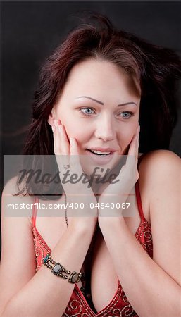 The young woman at the center of the frame. She is surprised and presses her hands to her face. On the one hand she has a bracelet. Black background.