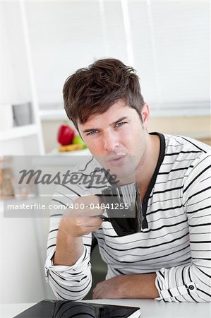 handsome man blowing on his cup of coffee sitting in the kitchen at home