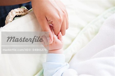 Close-up of a young mother holding her baby's hand at home