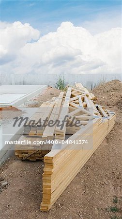 stack of wooden joists and building lumber at construction cite against a blue sky.