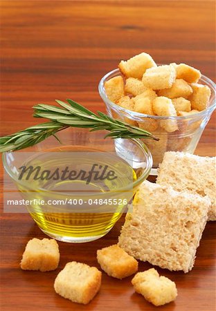 Two jars of olive oil with stick of rosemary and croutons on wooden table background