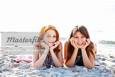 Two beautiful girls lie on the beach.