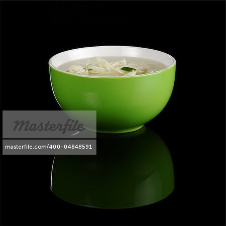 Chinese noodle soup in a green bowl photographed on black with a reflection