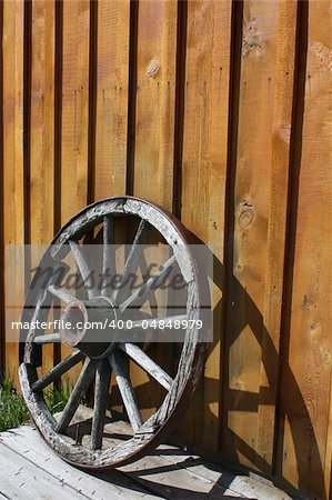 Abandoned wagon wheel against a wooden wall