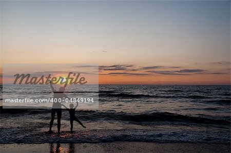 Silhouettes of father and his douther jumping and having fun on beach at sunset