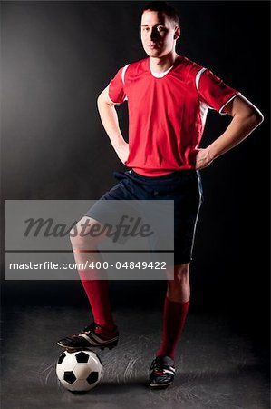 soccer player is standing with ball on dark background