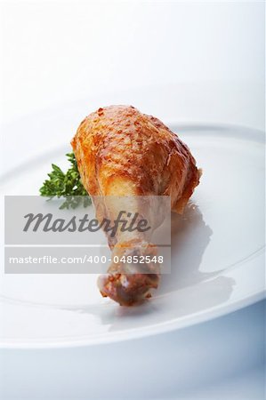 Closeup picture of roasted chicken leg on the white plate.