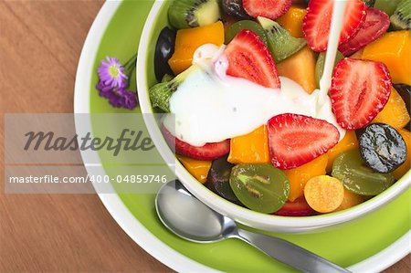 Fresh and healthy fruit salad with strawberry, kiwi, grape, mango and physalis in a bowl with plain yoghurt being poured over