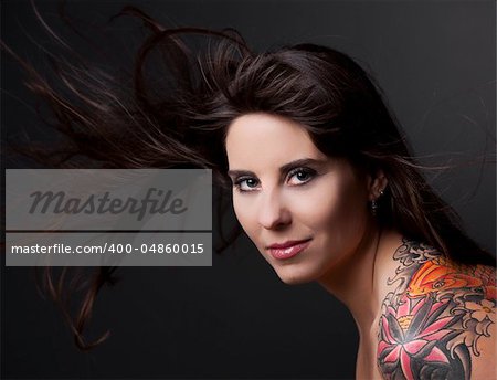 Portrait of a lovely woman with a tatto on the shoulder against a grey background and spread hair