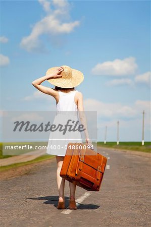 Lonely girl with suitcase at country road.