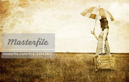 Redhead enchantress with umbrella and suitcase at spring wheat field. Photo in old image style.