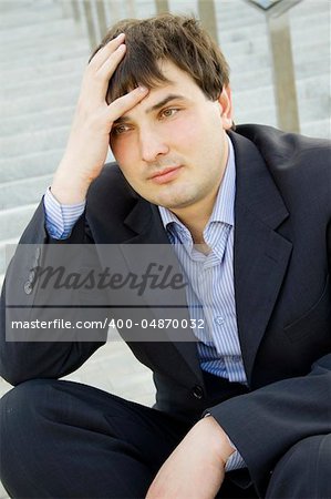 Closeup of a young businessman sitting on thethe stairs of of the building . Dismissed, frustrated