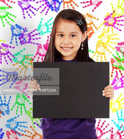 Young Cheerful Girl With A Blank Board And Wall With Colored Hands In The Background
