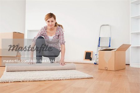 Pretty blonde woman rolling up a carpet to prepare to move house