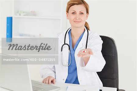 Smiling female doctor showing pills to the camera while sitting in her office