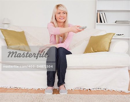 Good looking blonde female watching tv while sitting on a sofa in the living room