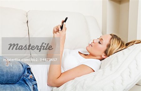 Pretty young woman lying on the couch and texting with her smartphone