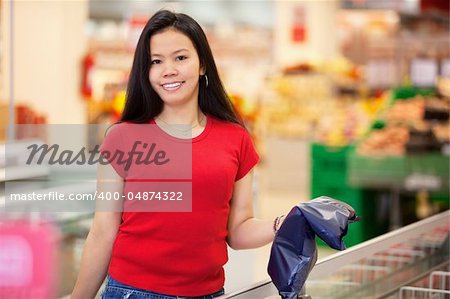 Smiling woman holding product in shopping centre and looking at camera