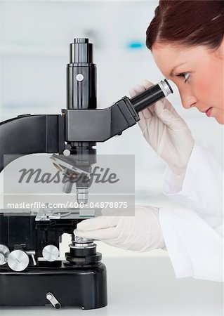 Beautiful red-haired scientist looking through a microscope in a lab