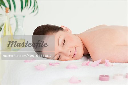 Beautiful woman lying on a massage table with petals and unlighted candles