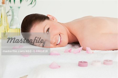 Smiling young woman lying on her belly with petals and unlighted candles