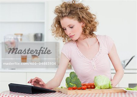 Pretty blonde woman relaxing with her tablet while cooking some vegetables in the kitchen in her appartment