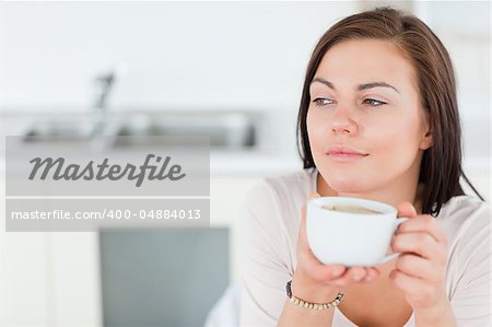 Close up of a smiling dark-haired woman having a coffee in her kitchen