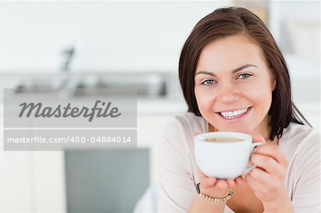 Close up of a smiling brunette having a coffee in her kitchen