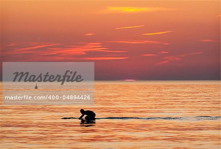 Surfer in the water at sundown against orange sky. Photo is taken at the beach in the west of The Netherlands.
