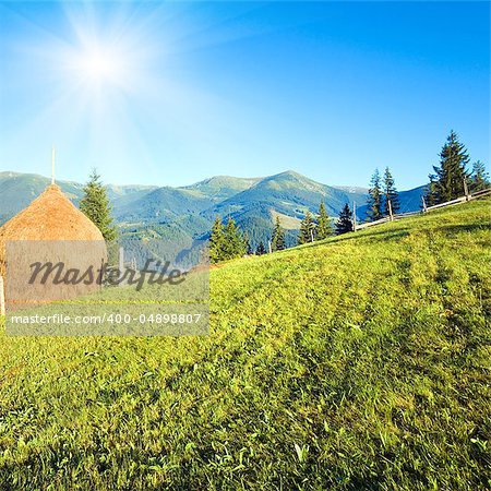 Summer mountain village outskirts with field haystack and sunshine