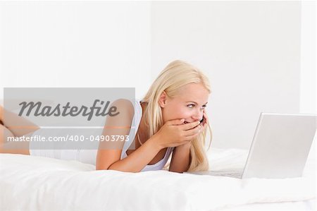 Woman laughing on the phone while using a laptop in her bedroom