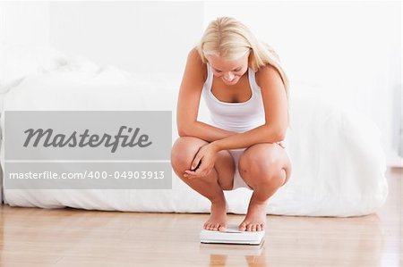 Fit woman on a weighing machine in her bedroom