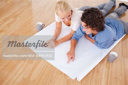 Man showing a point on a plan to his girlfriend while lying on the floor