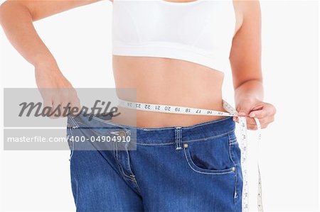 Woman measuring her waist while wearing too big jeans in a studio