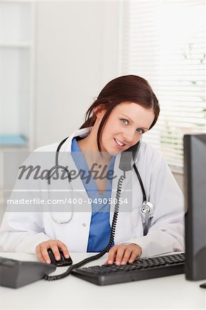 A female doctor is working with her pc and telephoning in her office