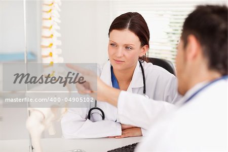 A doctor is showing a female doctor something on a spine