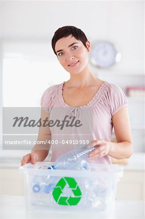 Cute brunette Woman putting bottles in a recycling box in a kitchen