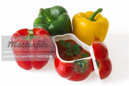 Red, green and yellow bell pepper with a ceramic ornament in shape of red pepper field with paprika ragout isolated on white background