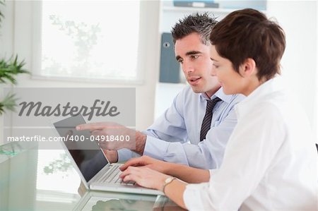 Man pointing at something to his secretary on a notebook in an office