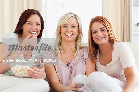Cheerful Women watching a movie eating popcorn in a living room