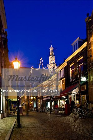 A cobble stone street with restaurants and shops leding towards the illuminated steeple of a big church at night