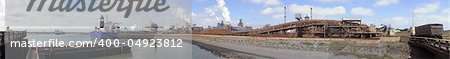 The downstream activities of a steel plant, with a huge crane unloading iron ore from a freight ship, and a lorry loading slag in an open trawler on a summer afternoon