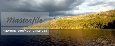 Sunlight illuminates the shoreline of Kintla Lake against a stormy sky in Glacier National Park - USA.