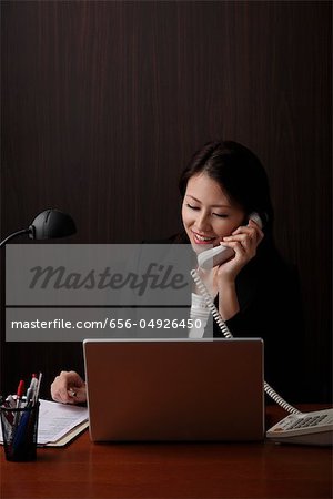 Chinese woman sitting at her desk and talking on phone.