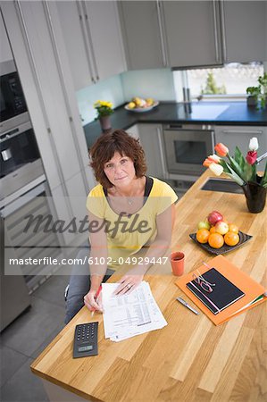Femme assise dans la cuisine avec factures, portrait