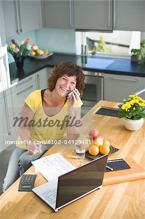 Femme assise avec factures et parler au téléphone mobile