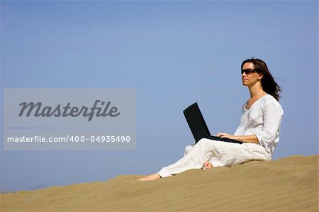 Girl working on her laptop in the dunes in Gran Canaria