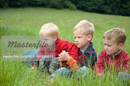 Three boyfriends sitting in the grass looking at something