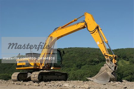 Yellow digger standing idle on a building construction site with rural countryside and a blue sky to the rear.