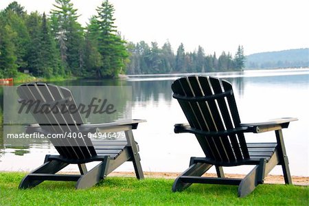 Two wooden chairs on a lake shore in the evening